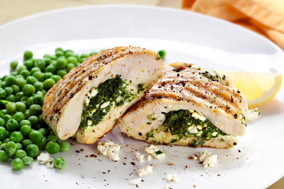 Un plato de pollo relleno con queso y espinaca acompañado por guisantes.