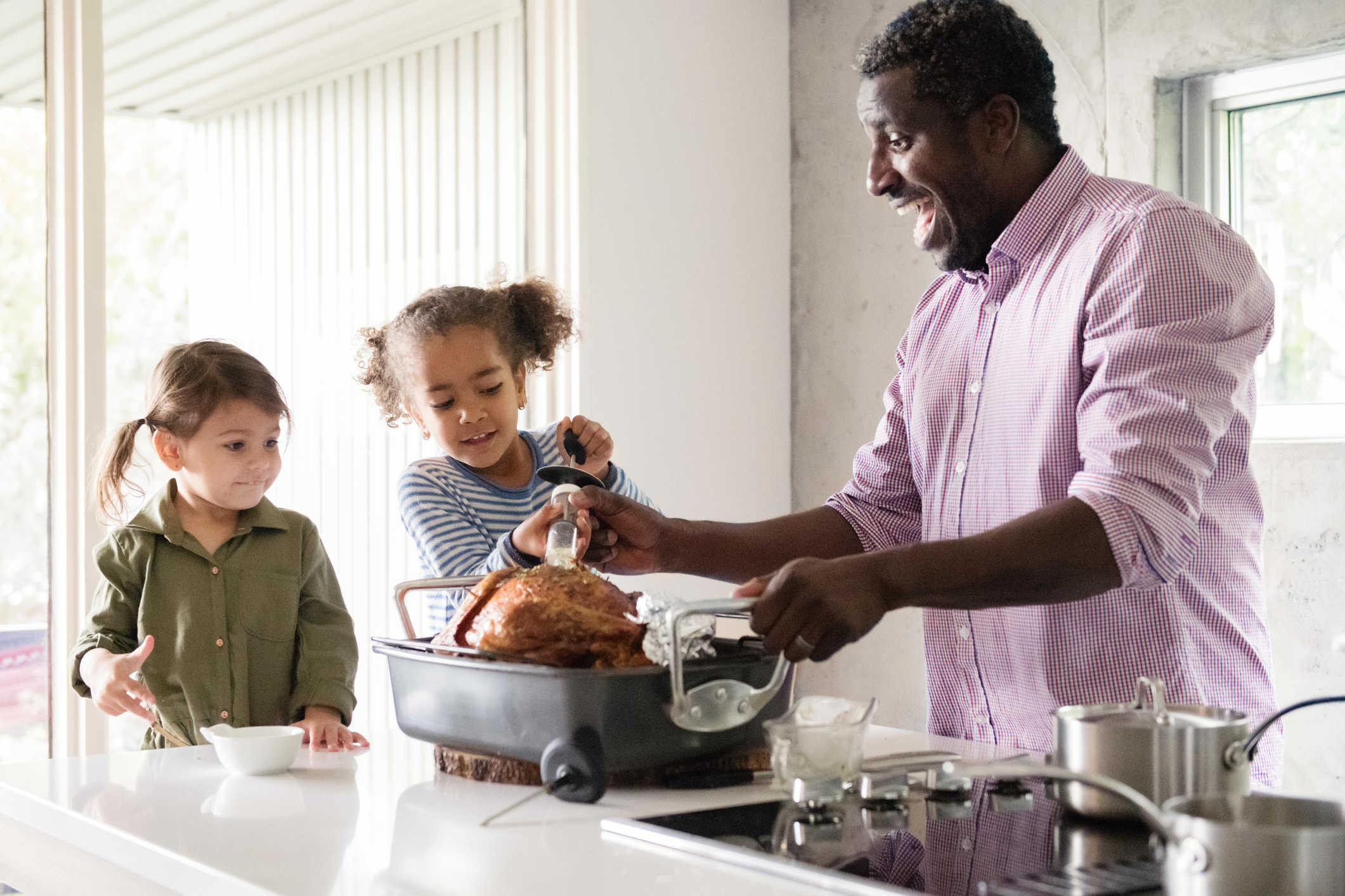 A father bastes a turkey on a counter with help from two young daughters.