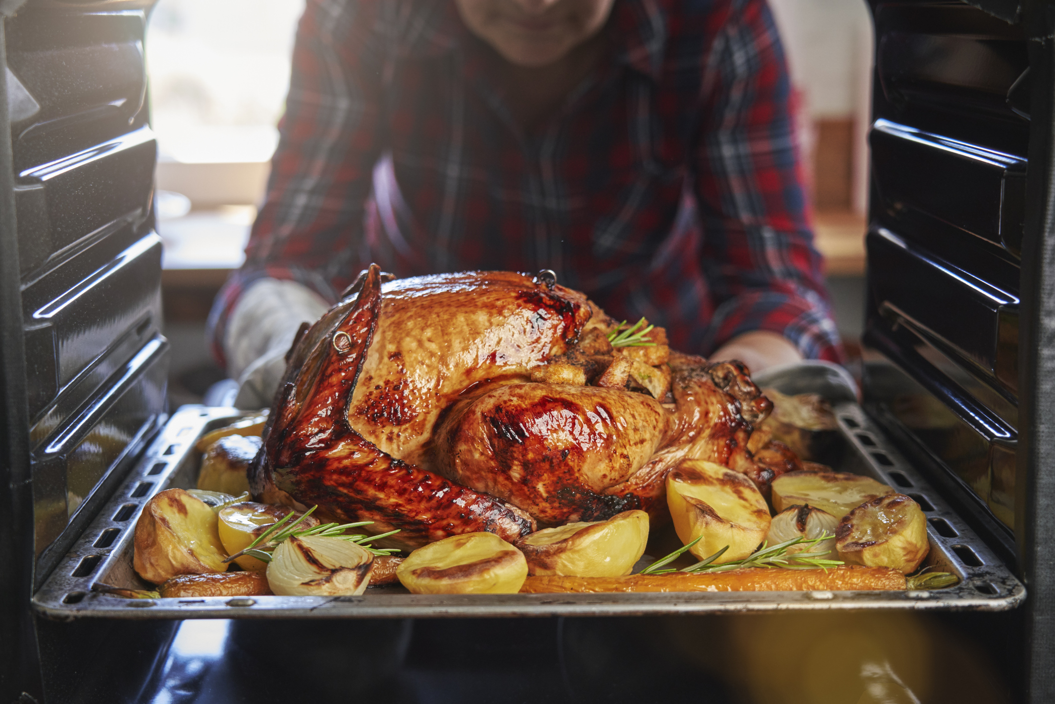 An photo from inside an oven of a person pulling a roast turkey and onions on a tray out of an oven.