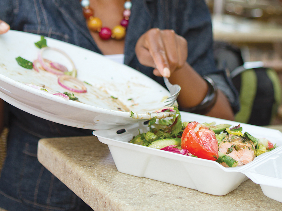 Una persona usa un tenedor para mover la comida de un plato a un recipiente para llevar.