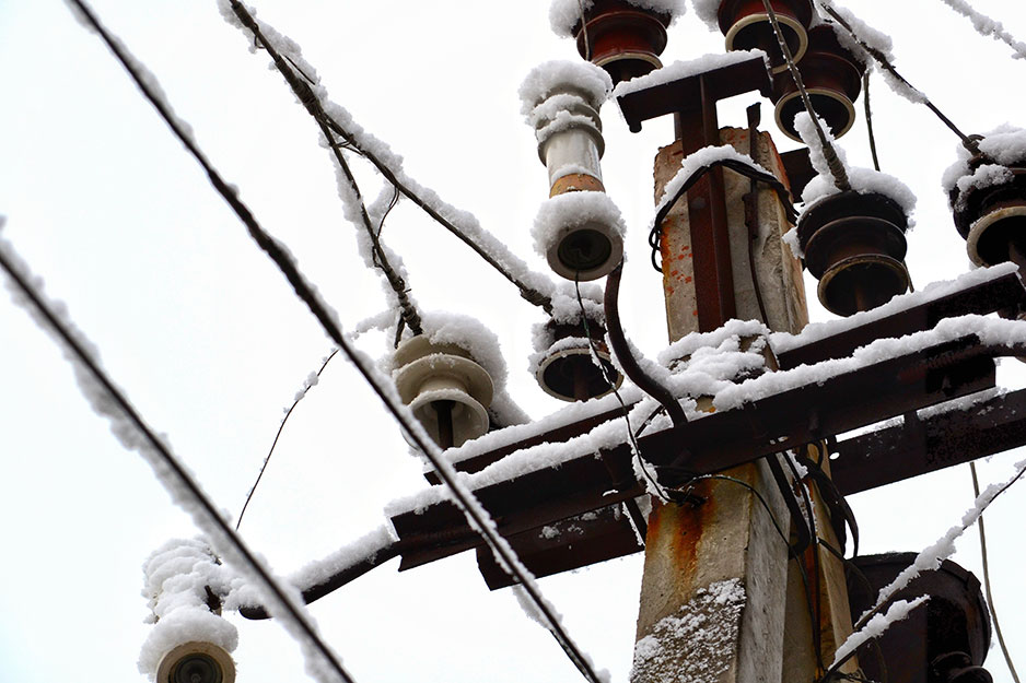 La parte superior de un poste eléctrico y cables cubiertos de nieve.