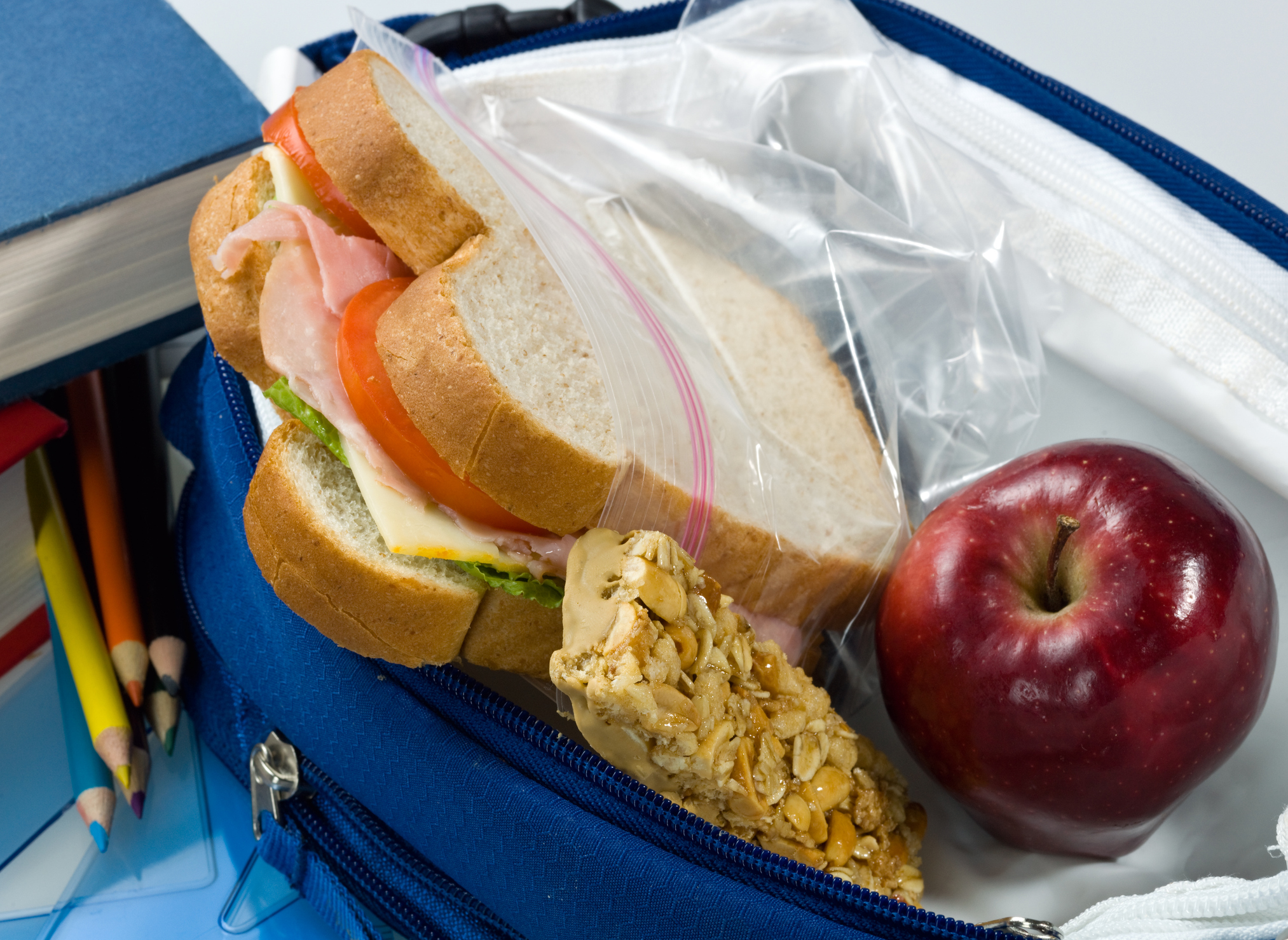 Un almuerzo para llevar con un sándwich, una barra de granola y una manzana.