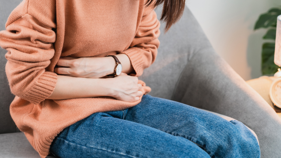 Person sitting hunched over, holding their stomach in discomfort.