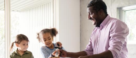 A father bastes a turkey on a counter with help from two young daughters.