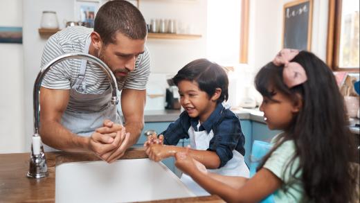 A man and his two children wash their hands in the kitchen sink.