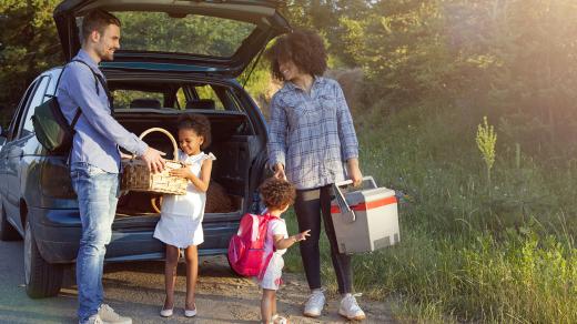 A family with two young children unpack coolers and snacks from the back of their car.