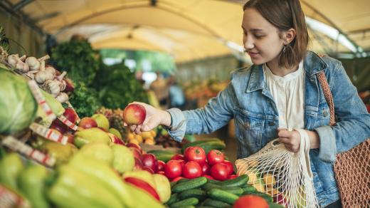 Woman shopping for apples at a covered farmers market booth.
