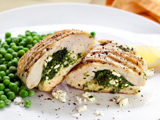 Un plato de pollo relleno con queso y espinaca acompañado por guisantes.