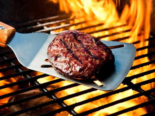 A seared hamburger on a grill spatula over a flame.