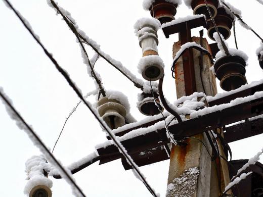 The top of an electrical pole and wires covered in snow.