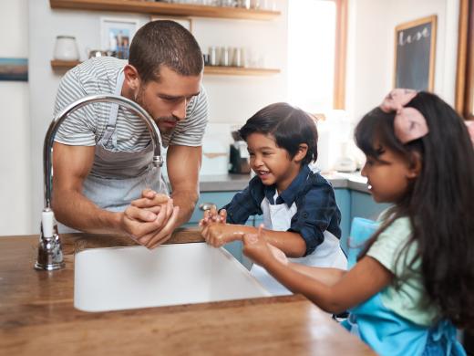A man and his two children wash their hands in the kitchen sink.