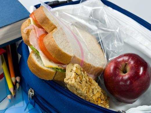 Un almuerzo para llevar con un sándwich, una barra de granola y una manzana.