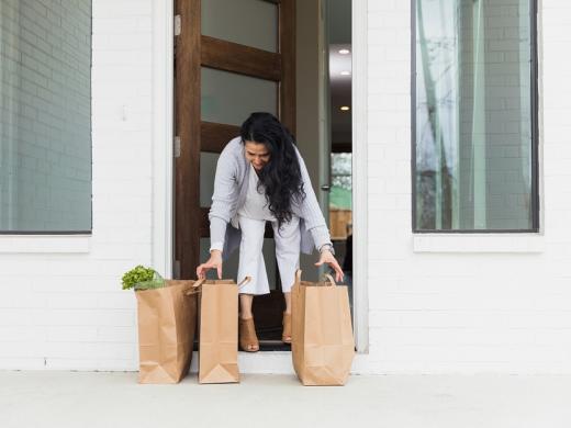 A women picks up groceries delivered on her doorstep.