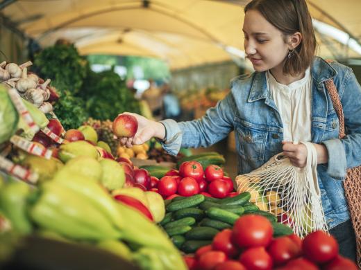 Woman shopping for apples at a covered farmers market booth.