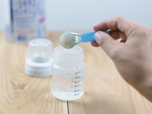 Powder milk and blue spoon on light background close-up.