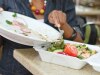 A person is using a fork to move food from a platter into a to-go container.