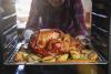 An photo from inside an oven of a person pulling a roast turkey and onions on a tray out of an oven.